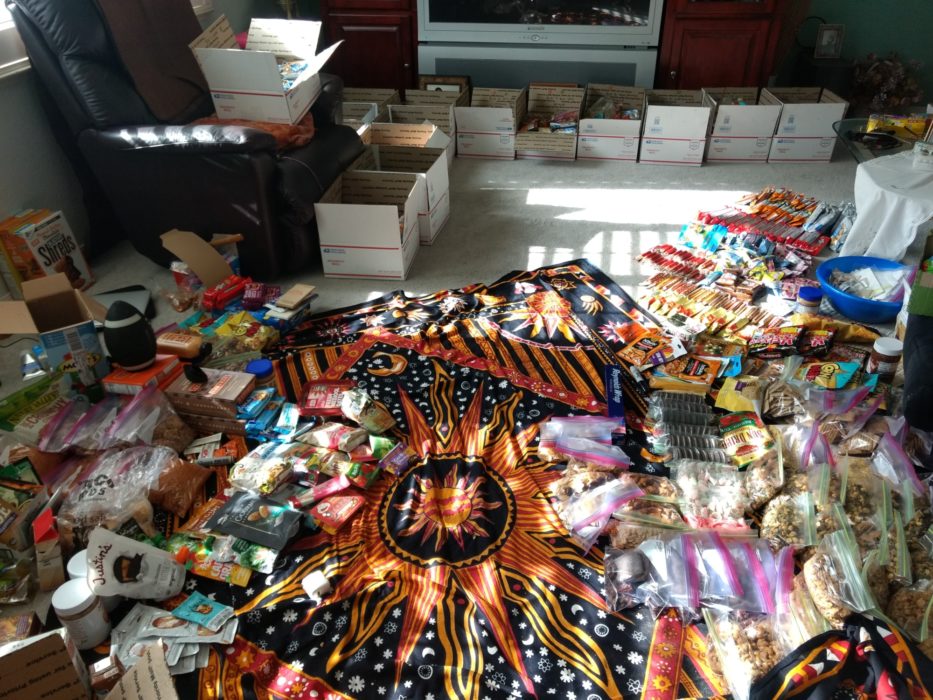 Resupply boxes: Food representing roughly 60 days of hunger prevention spreads across the living room floor before being carefully packaged in resupply boxes.